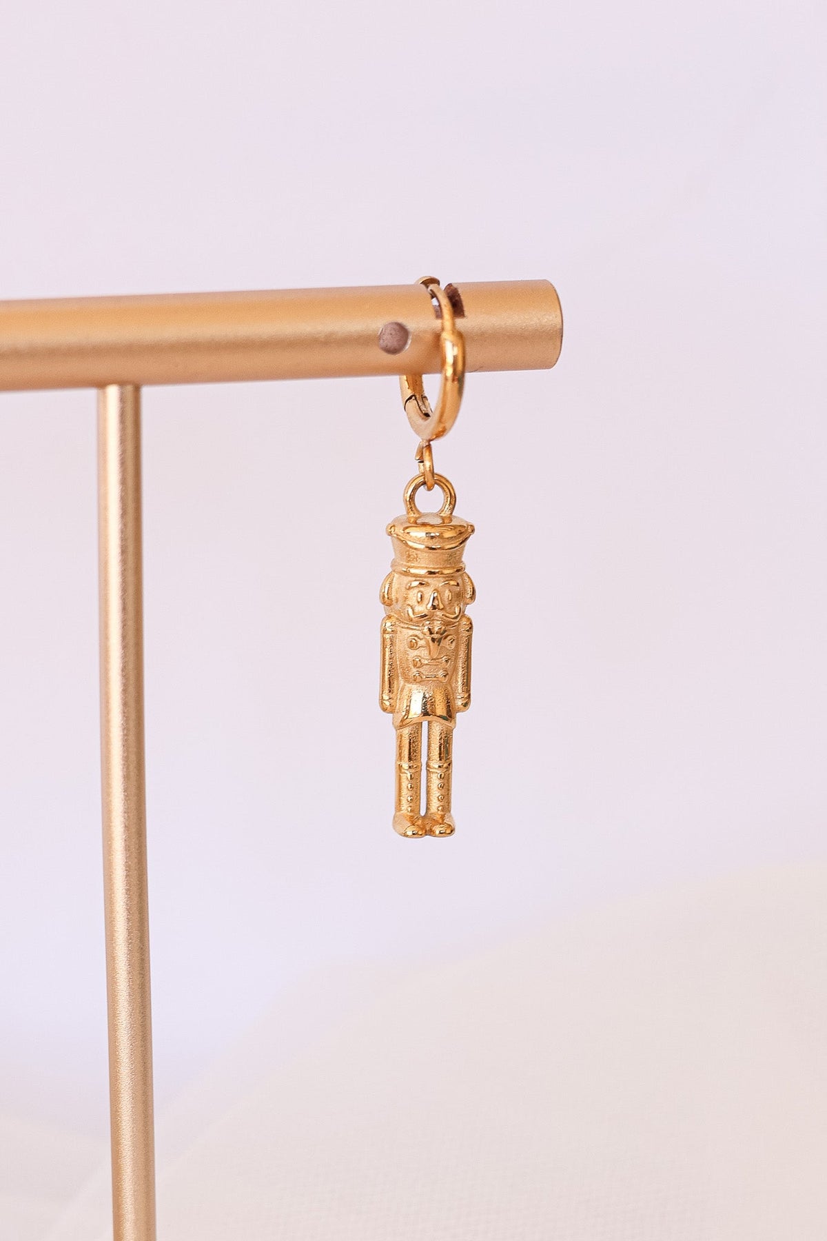 Gold Nutcracker Huggie Hoop earring with a dangling nutcracker charm