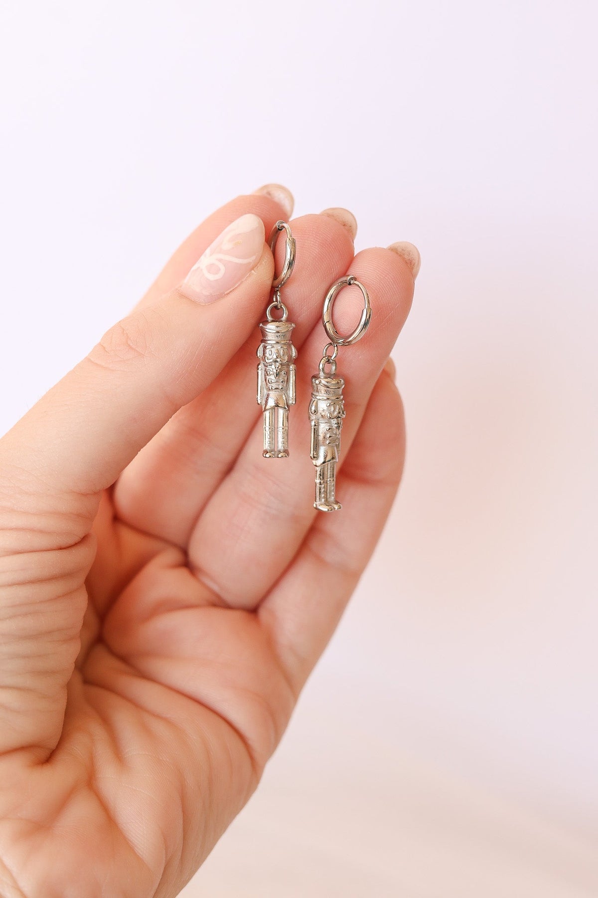 Pair of silver nutcracker huggie hoops held in a hand