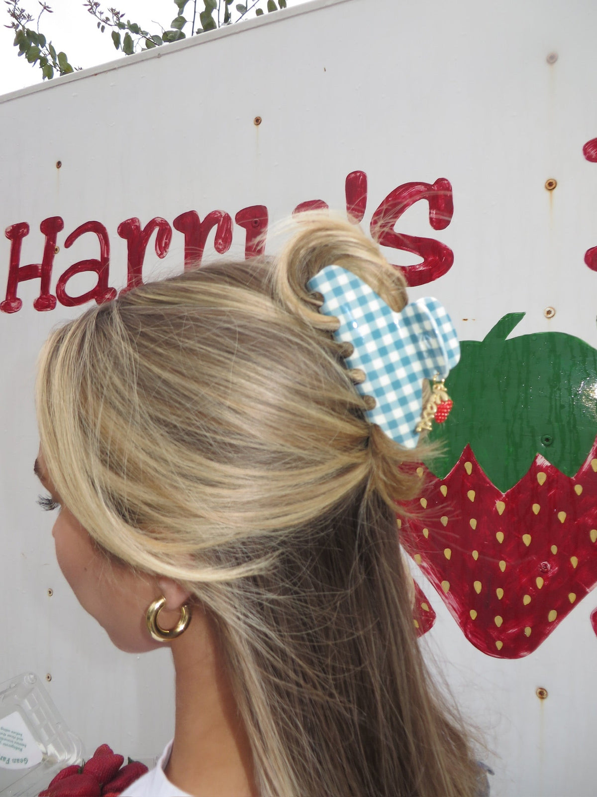 Blue gingham claw hair clip with red strawberry charm on blonde hair.
