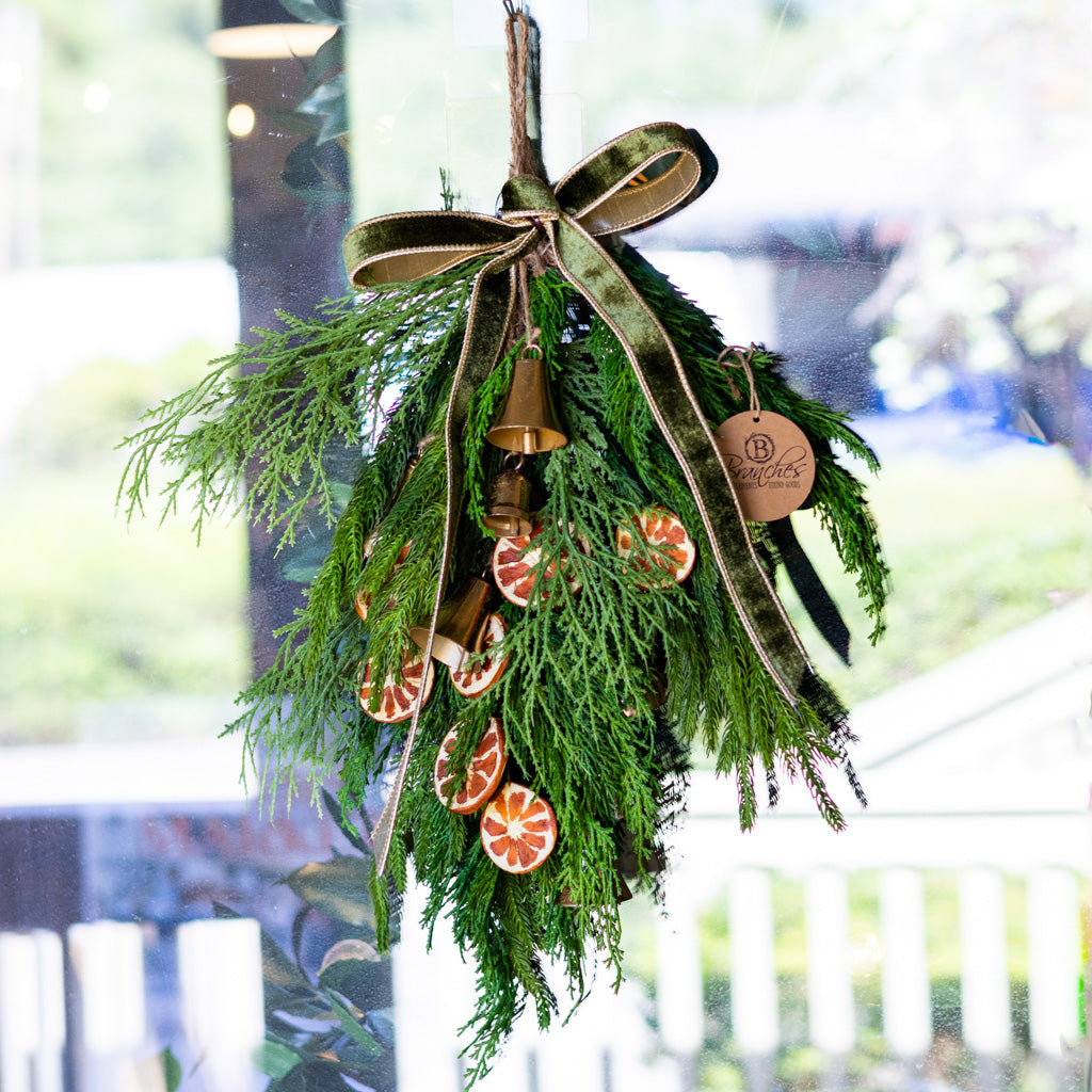 Hanging pine wreath with gold bells and orange slice ornaments, green ribbon and tag