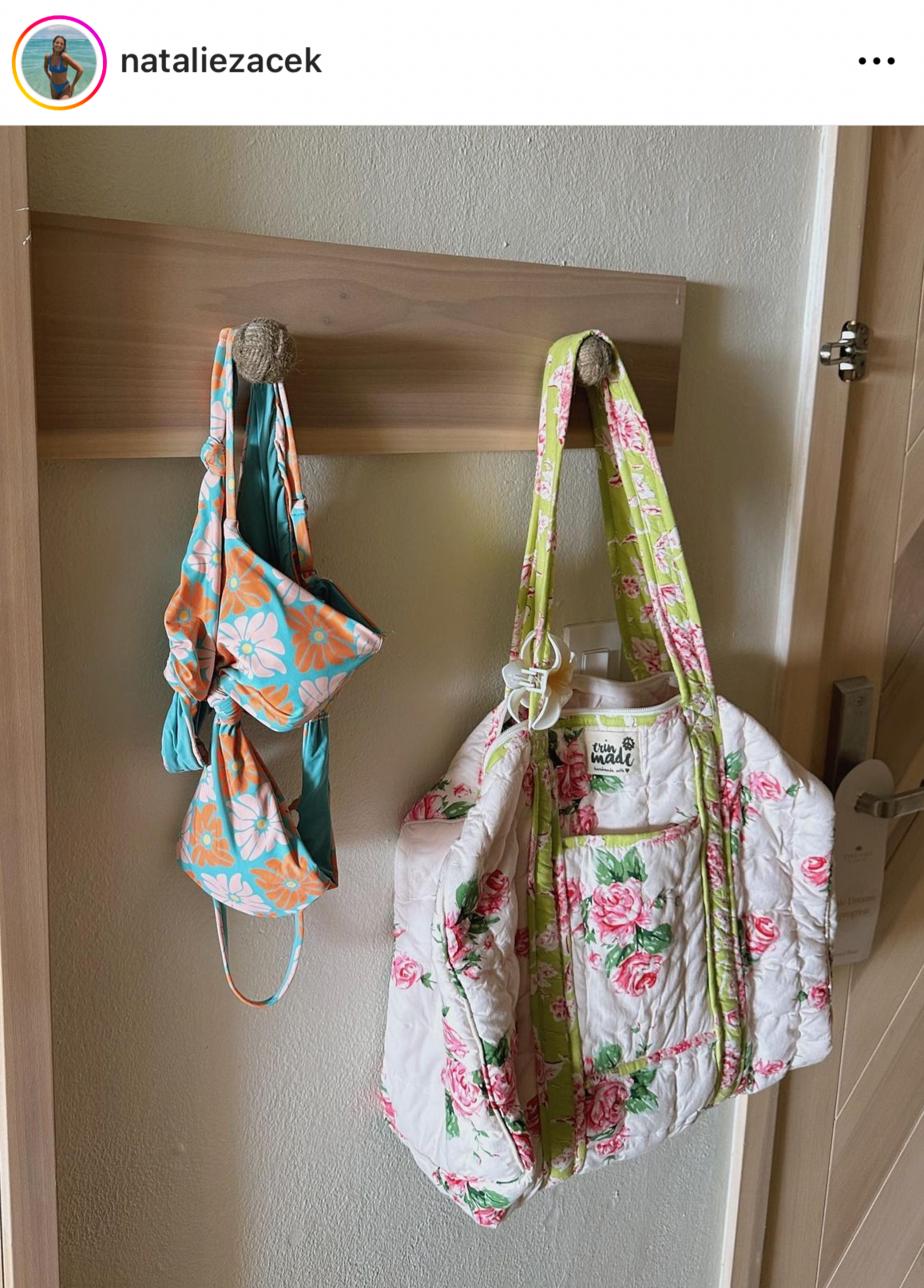 Floral white duffle bag with green trim and zip pocket, hanging from two handles
