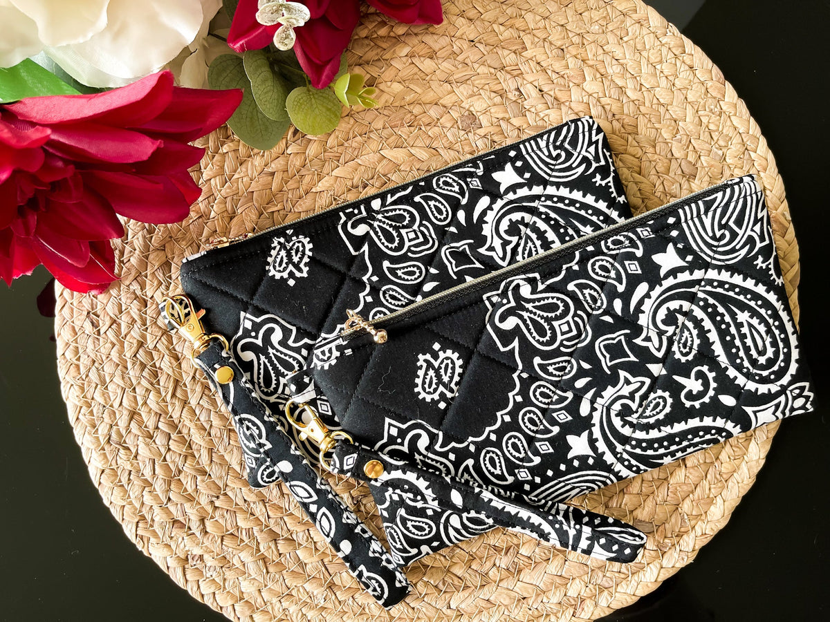 Quilted wristlet pouch with paisley print and gold chain wrist strap across the front