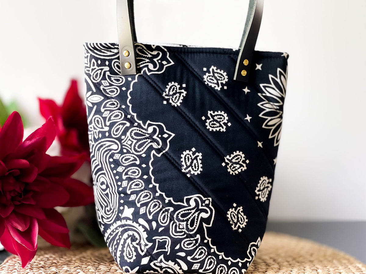 Navy bucket bag with white paisley print, diagonal stitched panel, gold grommets and handles.