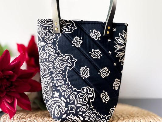 Navy bucket bag with white paisley print, diagonal stitched panel, gold grommets and handles.