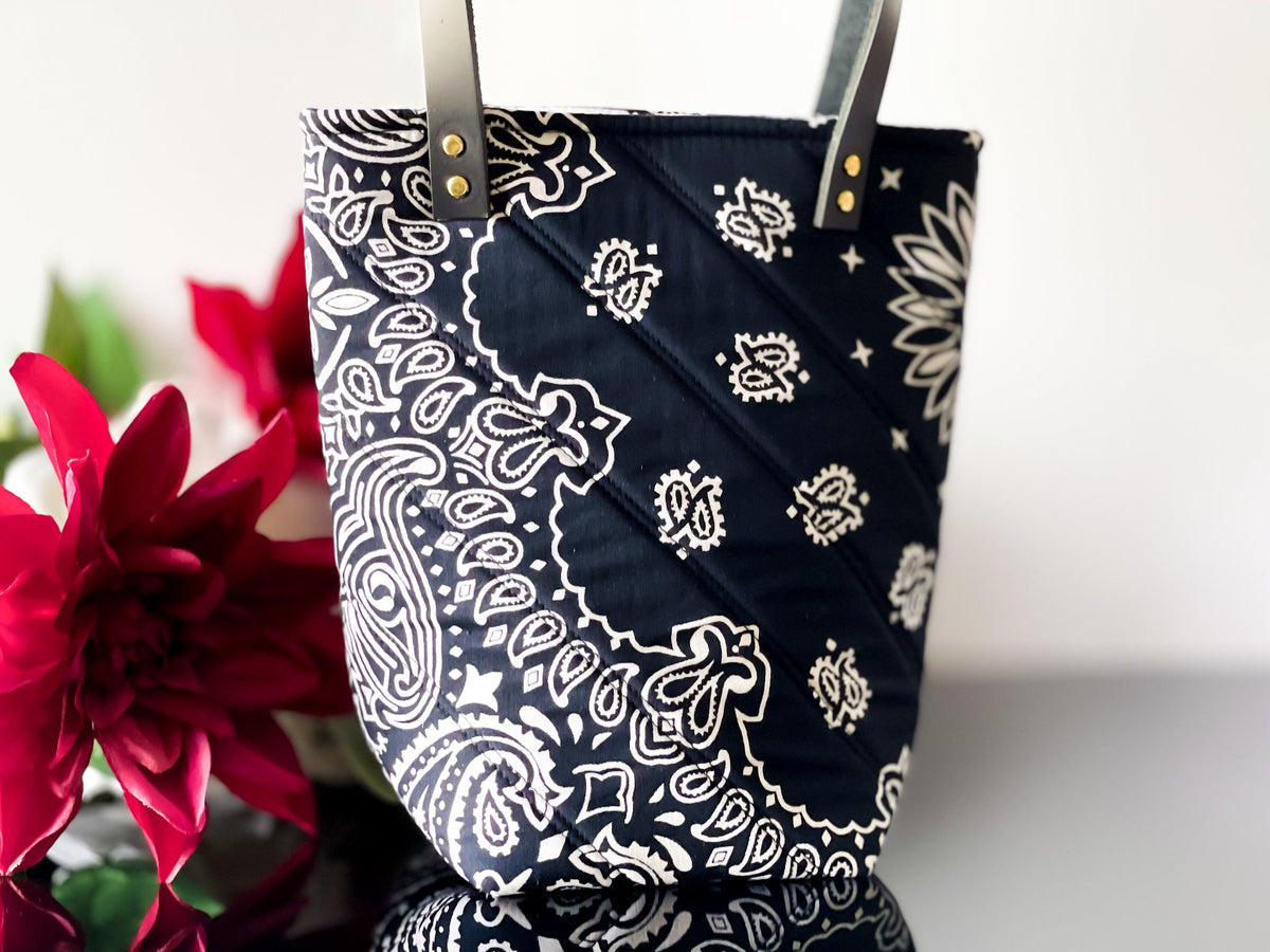 Navy bucket bag with white paisley print, front cross-stitch panel and gold grommets.