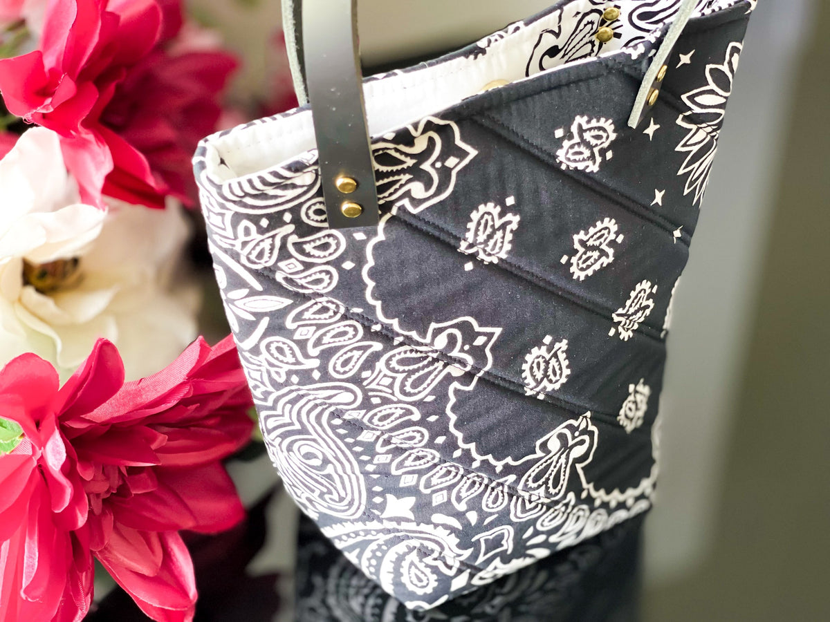 Navy bucket bag with white paisley print, top handle with gold rivets, partly open top.