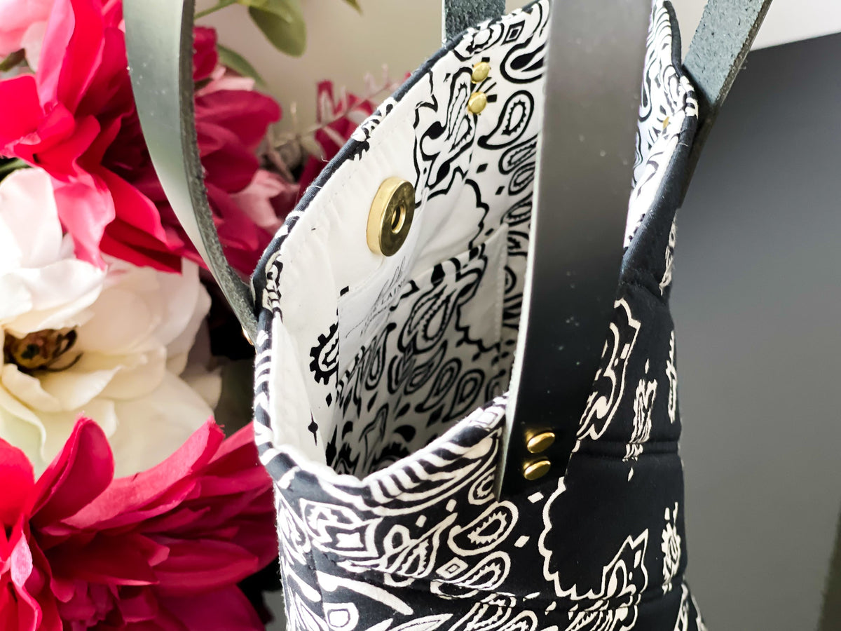 Navy bucket bag with white paisley lining, gold button detail and side handle hardware.