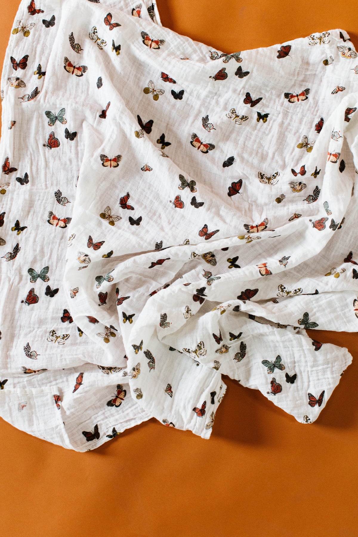 White muslin swaddle blanket draped close-up, multicolor butterfly print