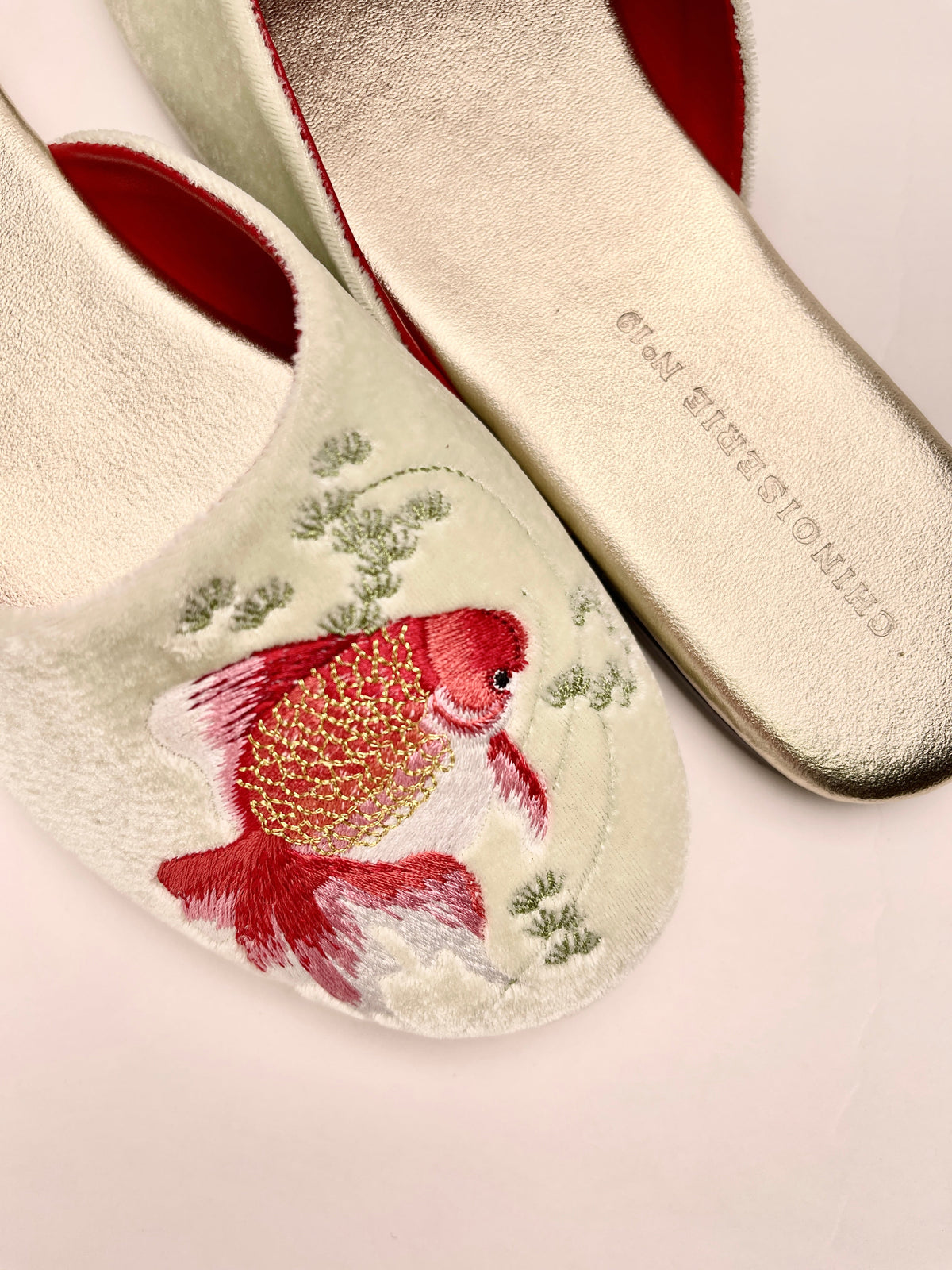 Close-up of mint velvet mule slippers with red goldfish and green floral embroidery