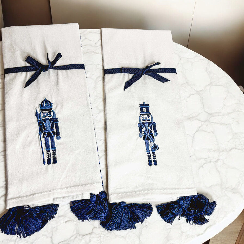Pair of off-white nutcracker tea towels with blue nutcracker applique and bow tie trim