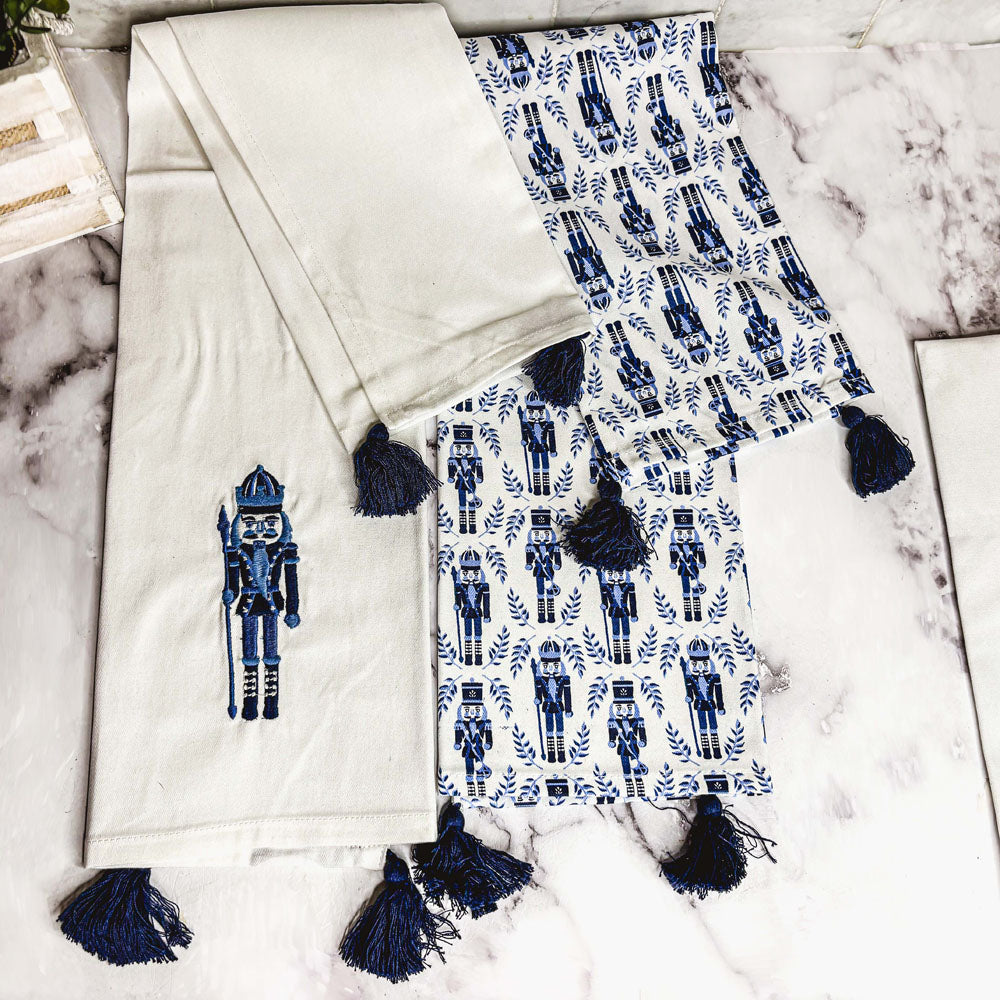 Blue nutcracker print tea towel with white background and navy tassel fringe