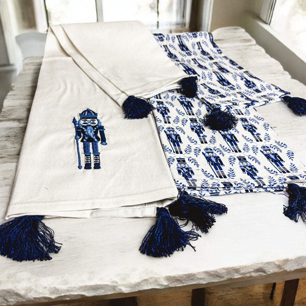 Nutcracker tea towel set on sofa: off-white towel with blue nutcracker and tassels