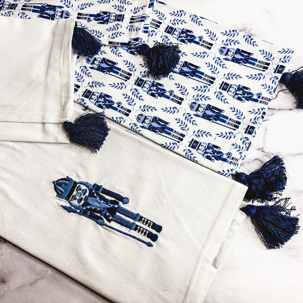 Blue nutcracker tea towel set with off-white towel, blue applique and tassel trim