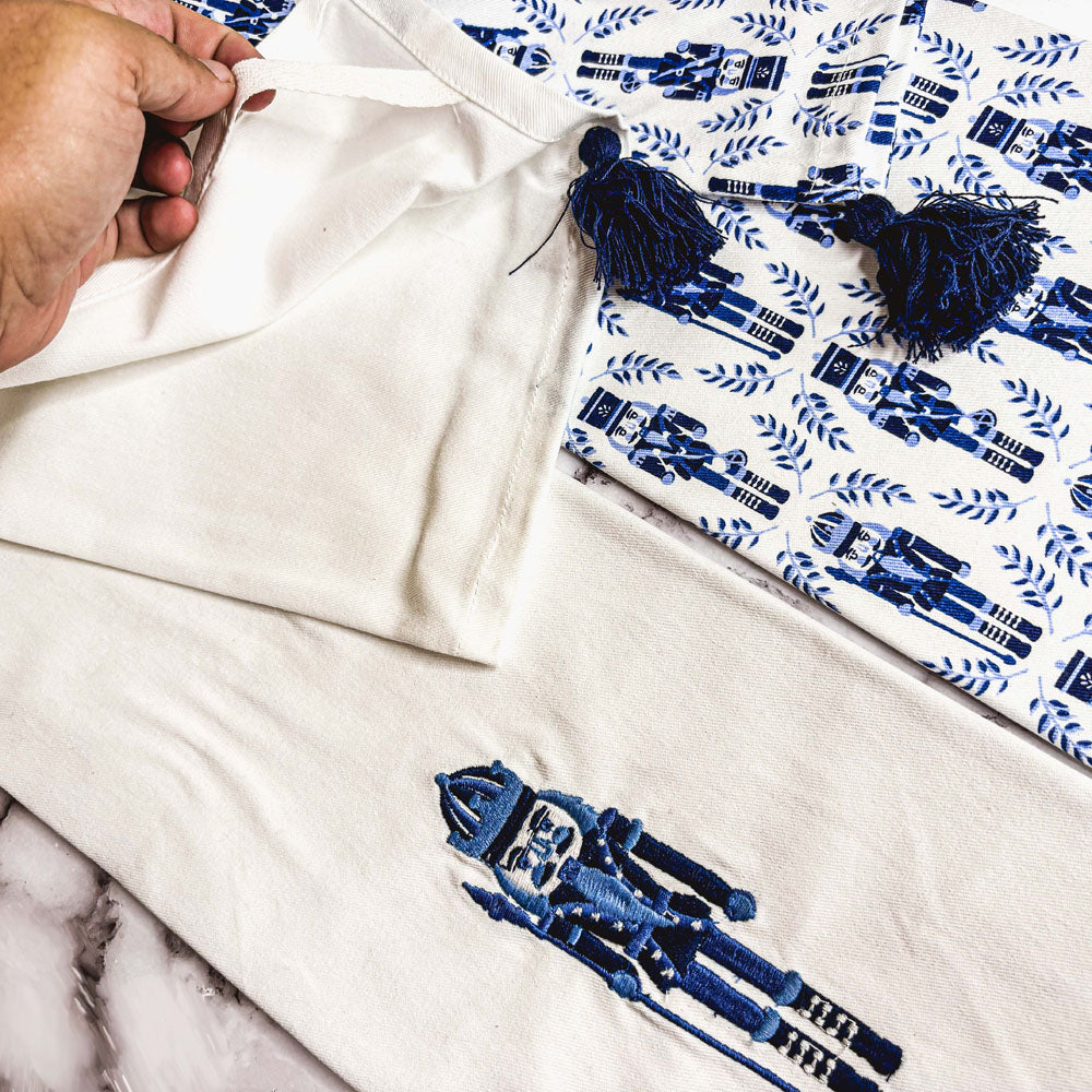 White tea towel edge detail with small blue nutcracker graphic and navy tassel