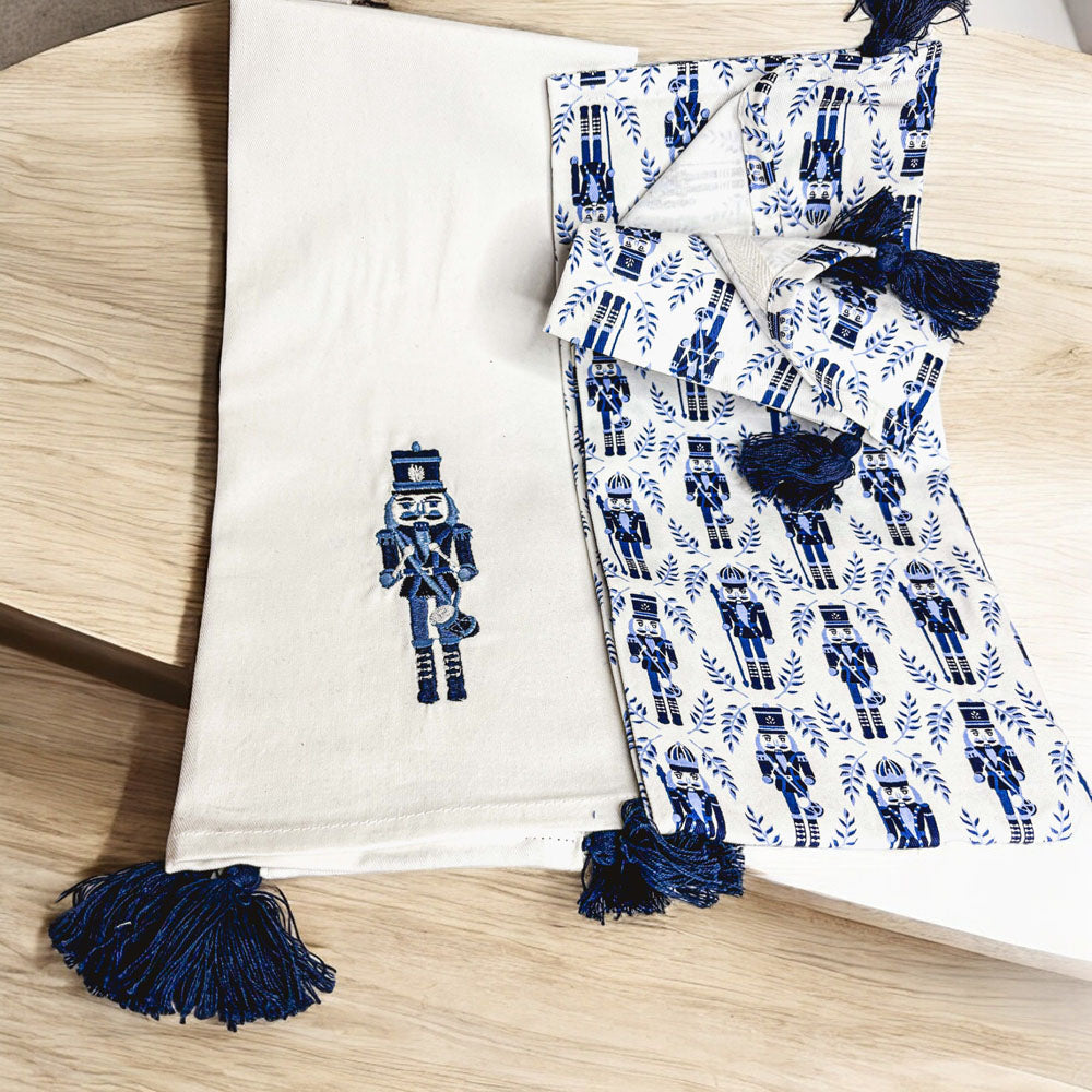 Nutcracker tea towel set: off-white towel with blue nutcracker and tassel fringe, patterned towel