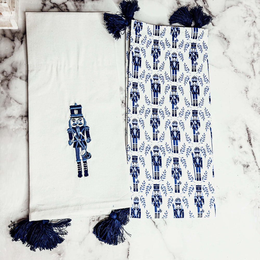 White tea towel with blue nutcracker motif and navy tassel fringe, folded style
