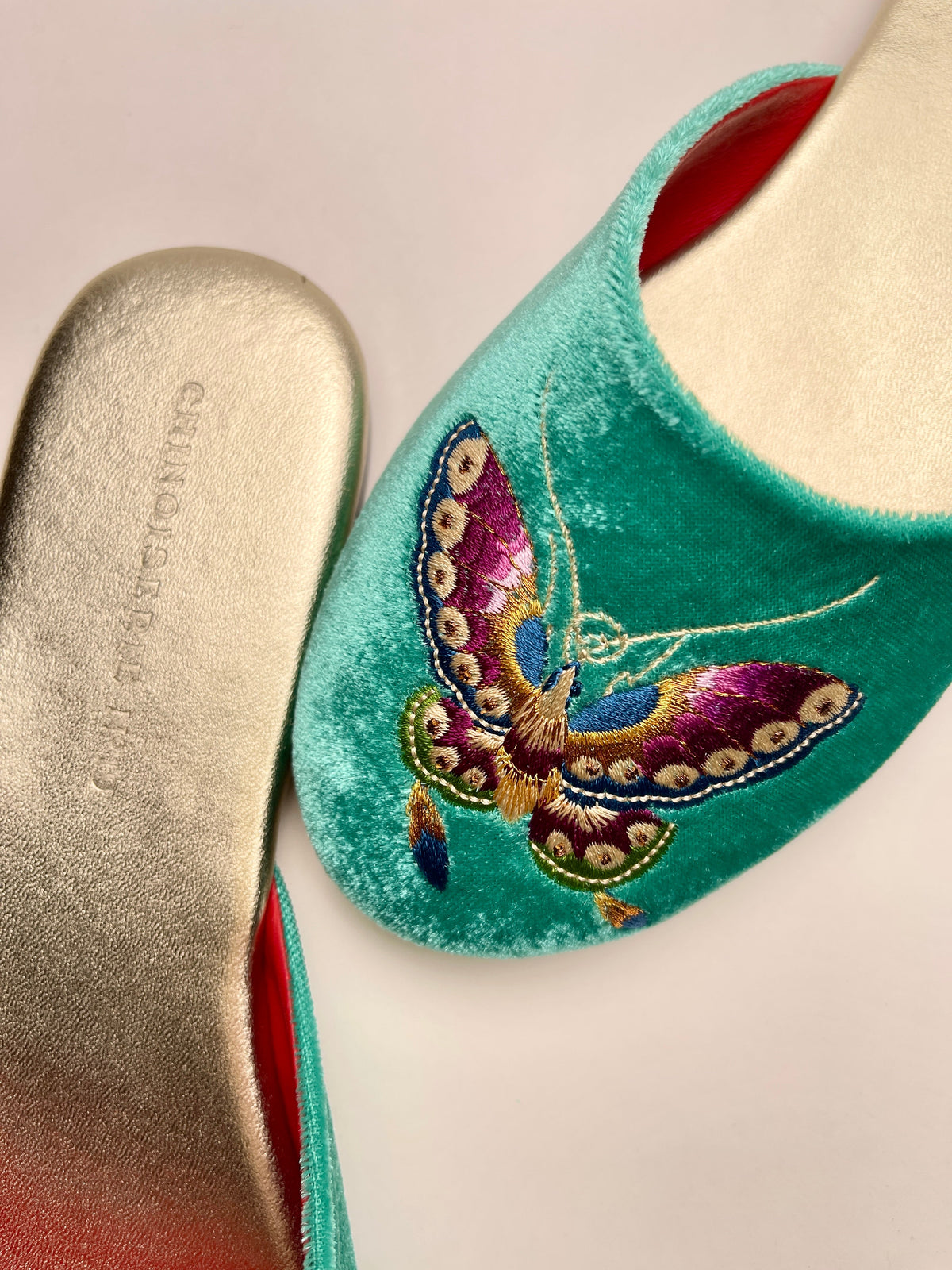 Jade green velvet mule slipper close-up with butterfly embroidery and red inner lining.