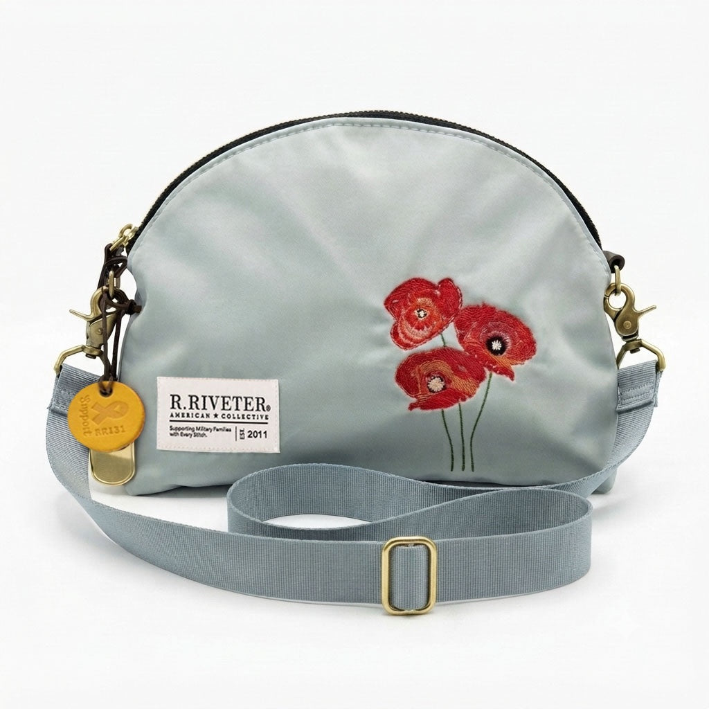 Light blue nylon crossbody bag with gold zipper, red embroidered poppies, logo patch and buckle strap