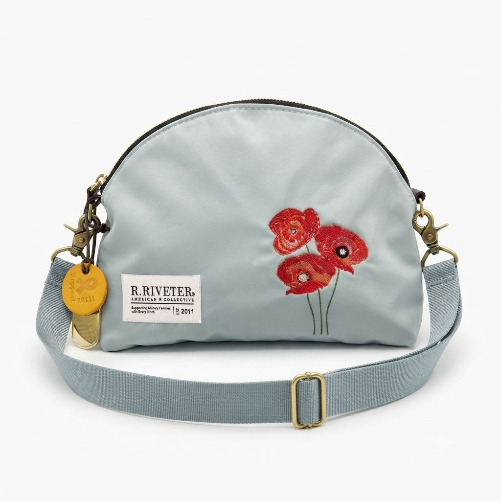 Light blue nylon crossbody bag with gold zipper, red embroidered poppies, front logo patch, strap