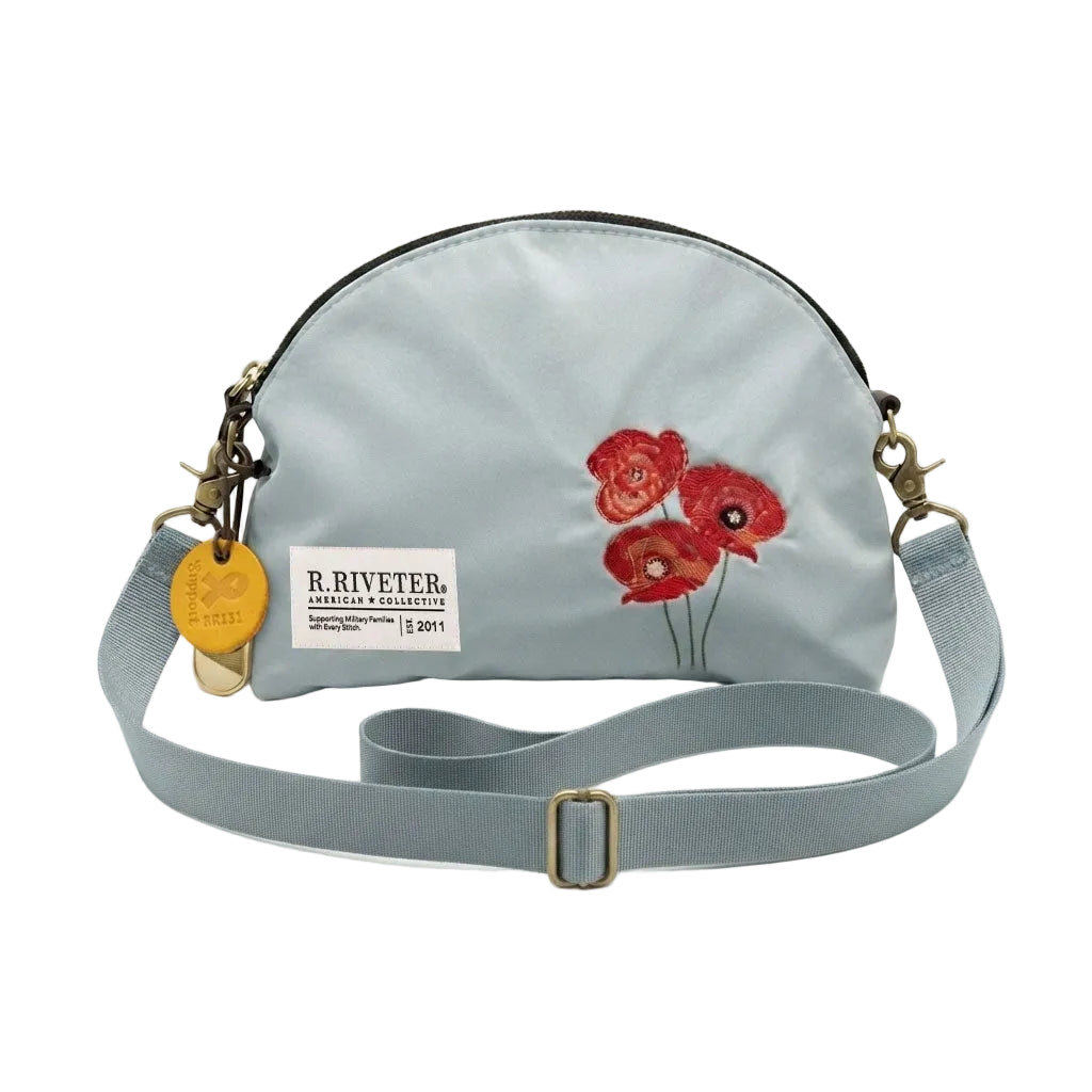 Light blue nylon crossbody bag with gold zipper, red embroidered poppies, logo patch and strap