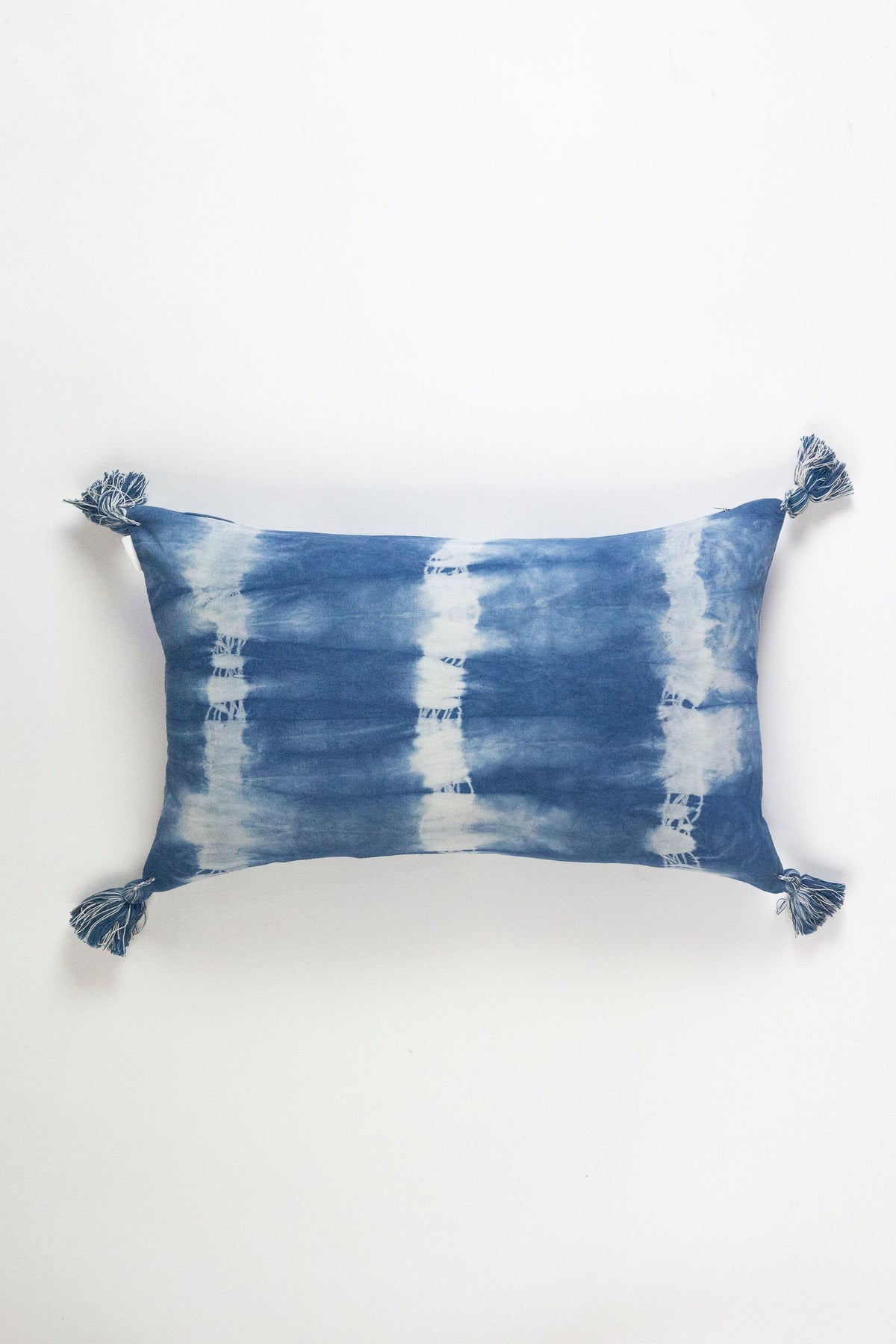Indigo shibori lumbar pillow with blue-and-white striped pattern and tassels
