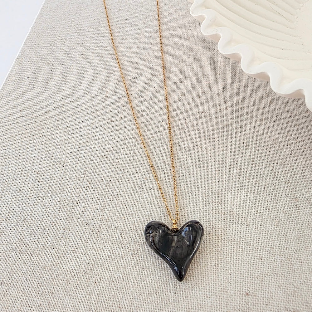 Black resin heart pendant necklace on gold chain, close-up