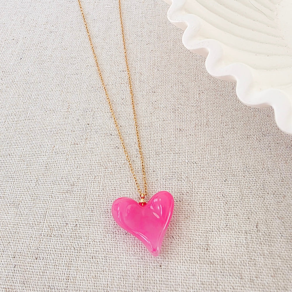 Pink resin heart pendant necklace on gold chain, close-up