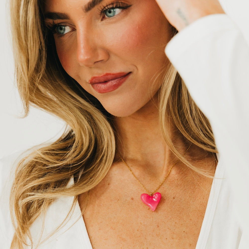 Pink resin heart pendant necklace with gold chain, close-up