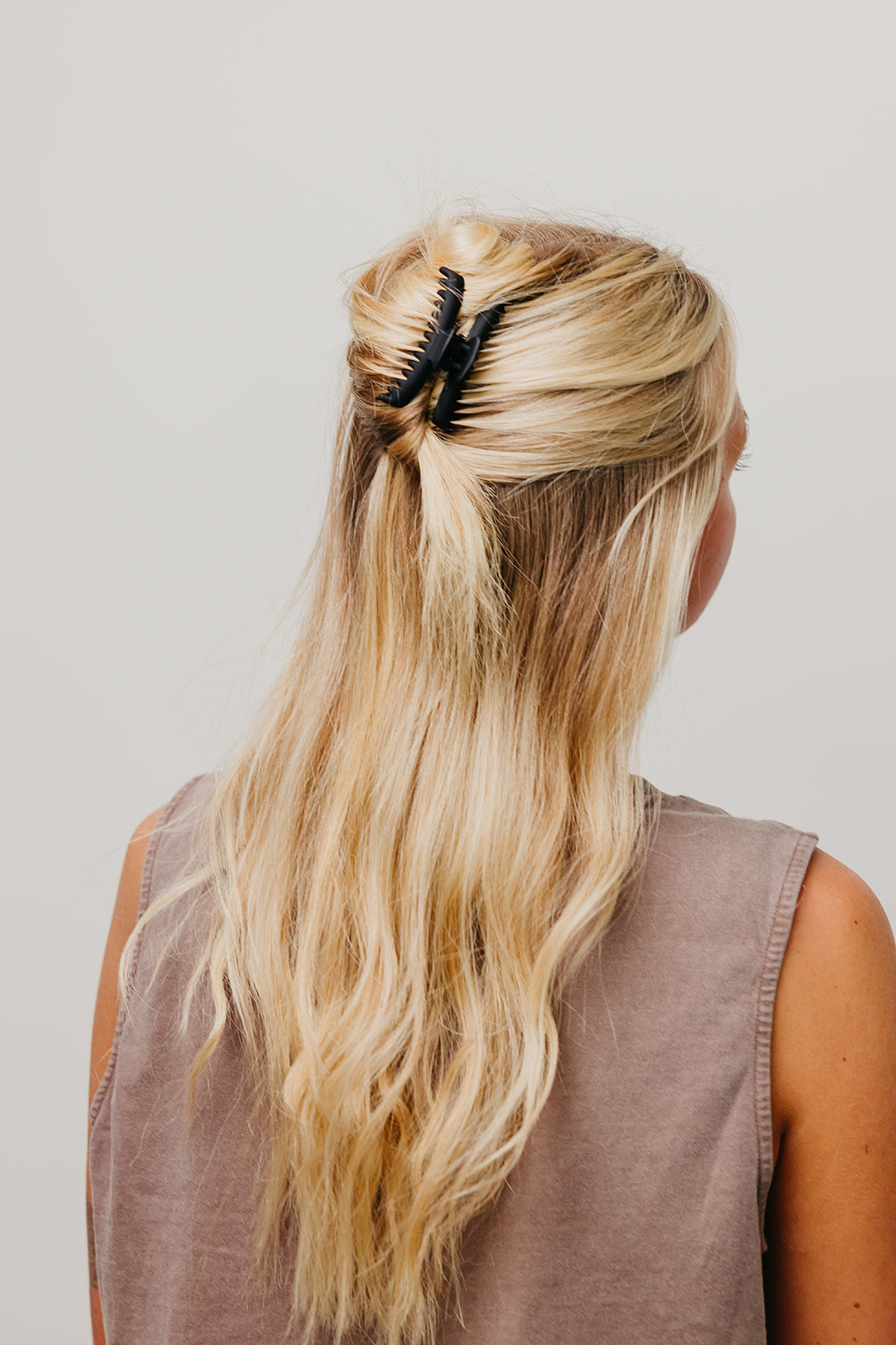 Black matte claw hair clip holding long blonde hair in a half-up bun.