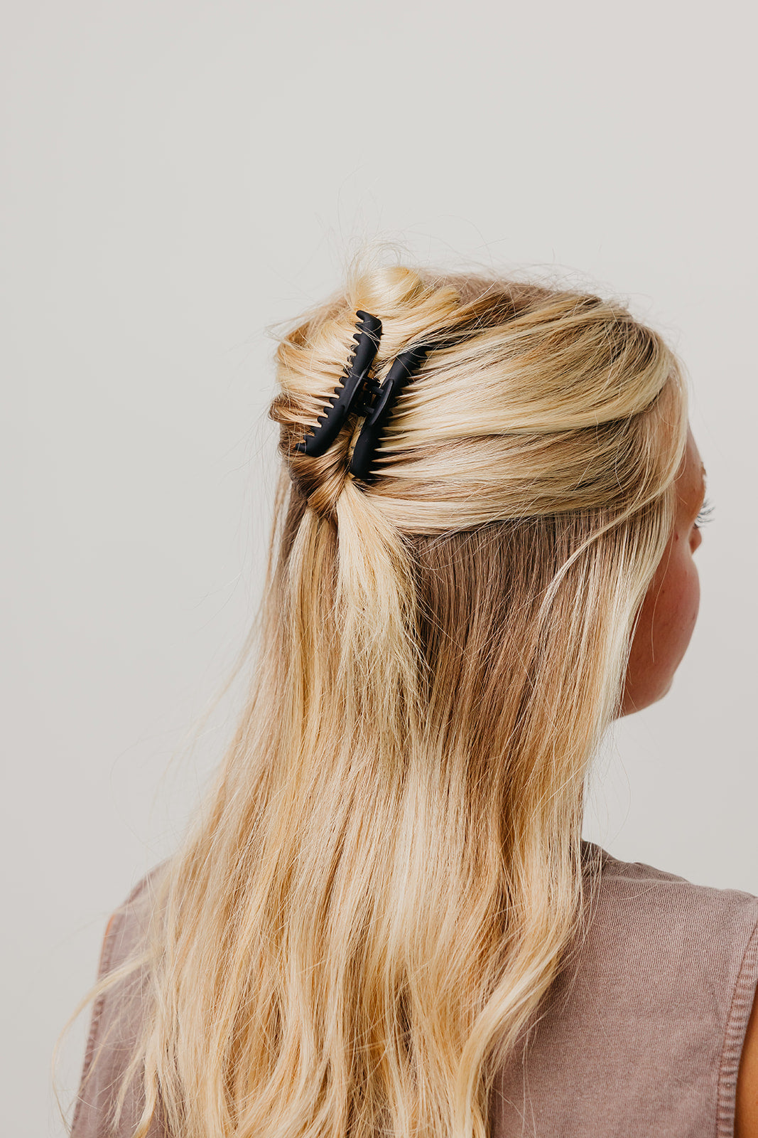 Black matte claw hair clip holding long blonde hair in a half-up style.