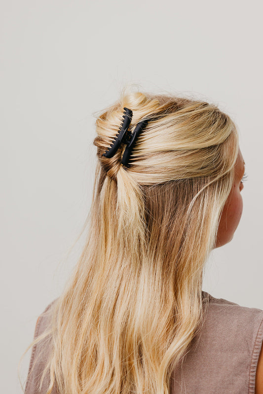 Black matte claw hair clip holding long blonde hair in a half-up style.