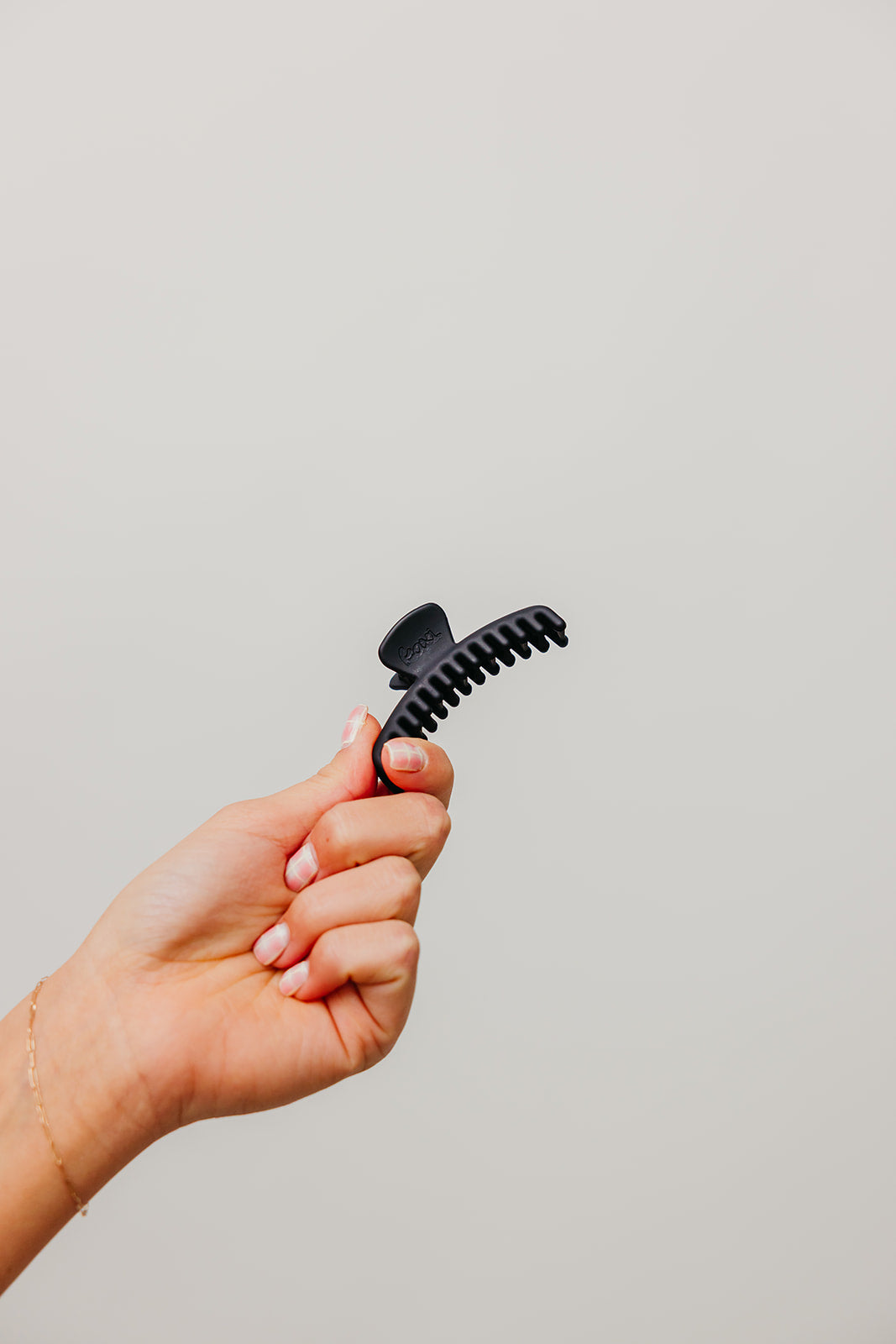 Hand holding a small black matte claw hair clip with curved teeth.