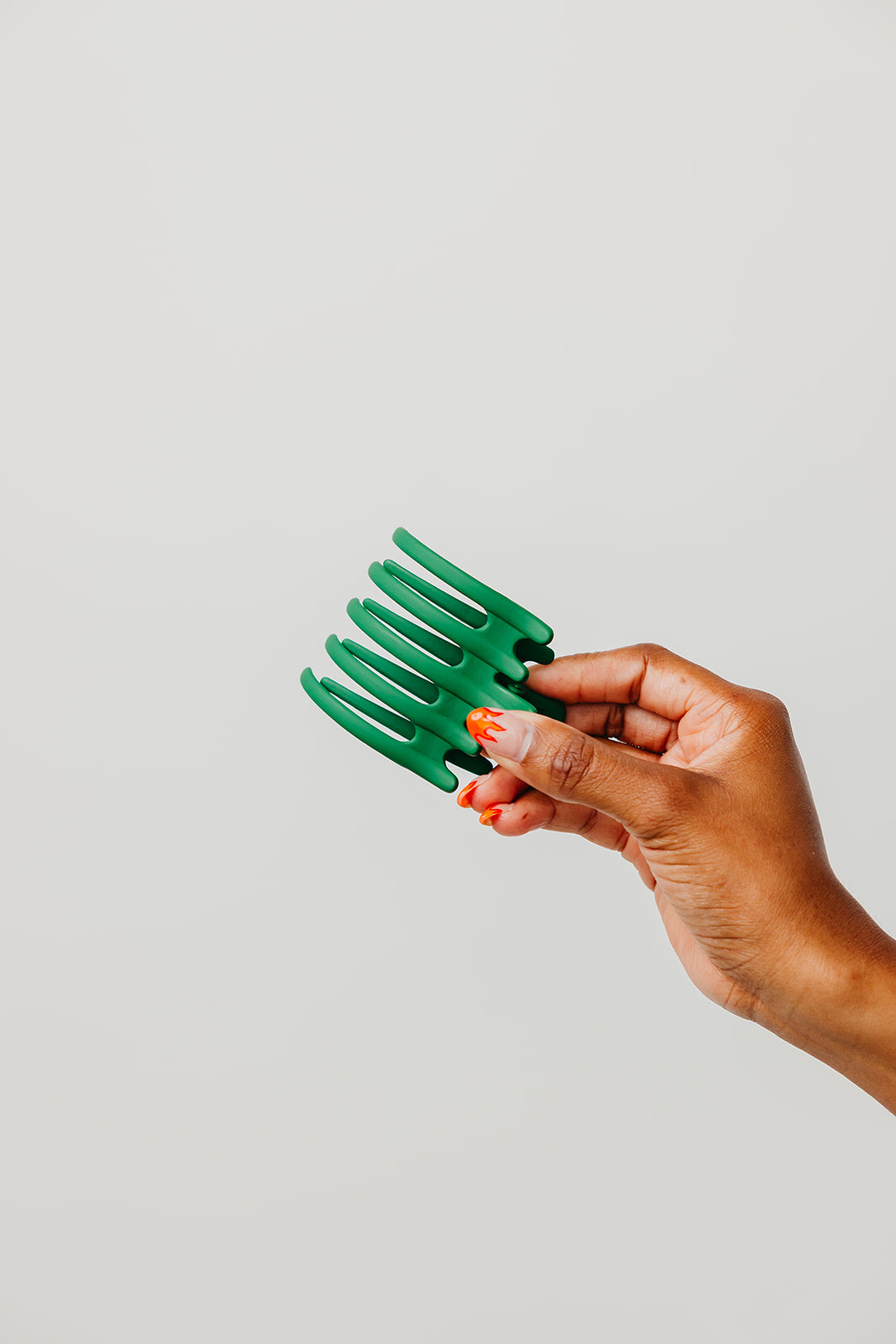 Wide hair claw clip in teal green, held in a hand