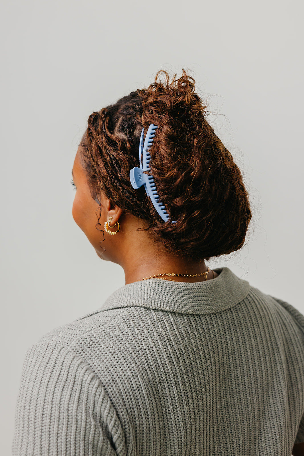Matte hair claw clip with comb teeth, in dark curly hair, back/side view; gray sweater.