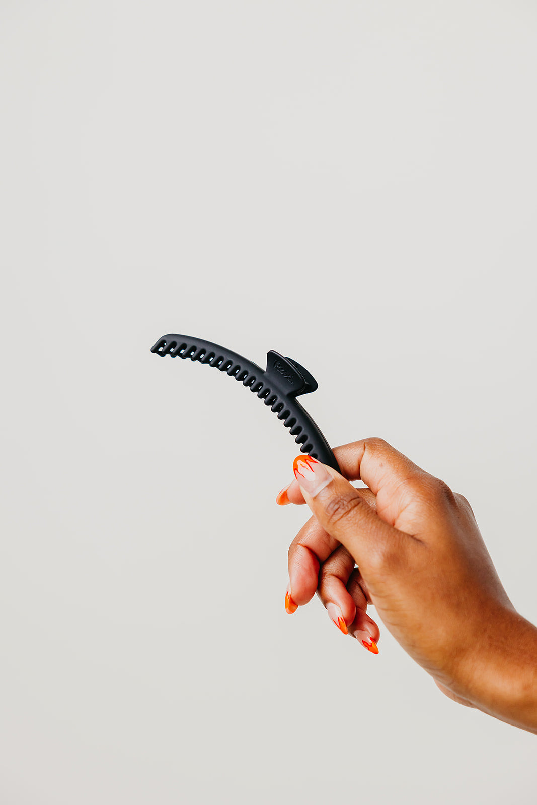 Hand holding matte black claw hair clip with curved comb teeth