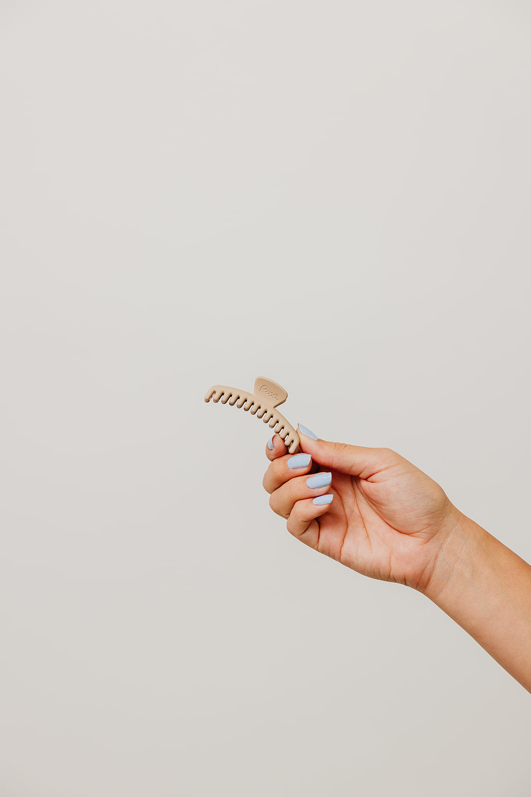 Matte mini claw hair clip in light tan, held by hand