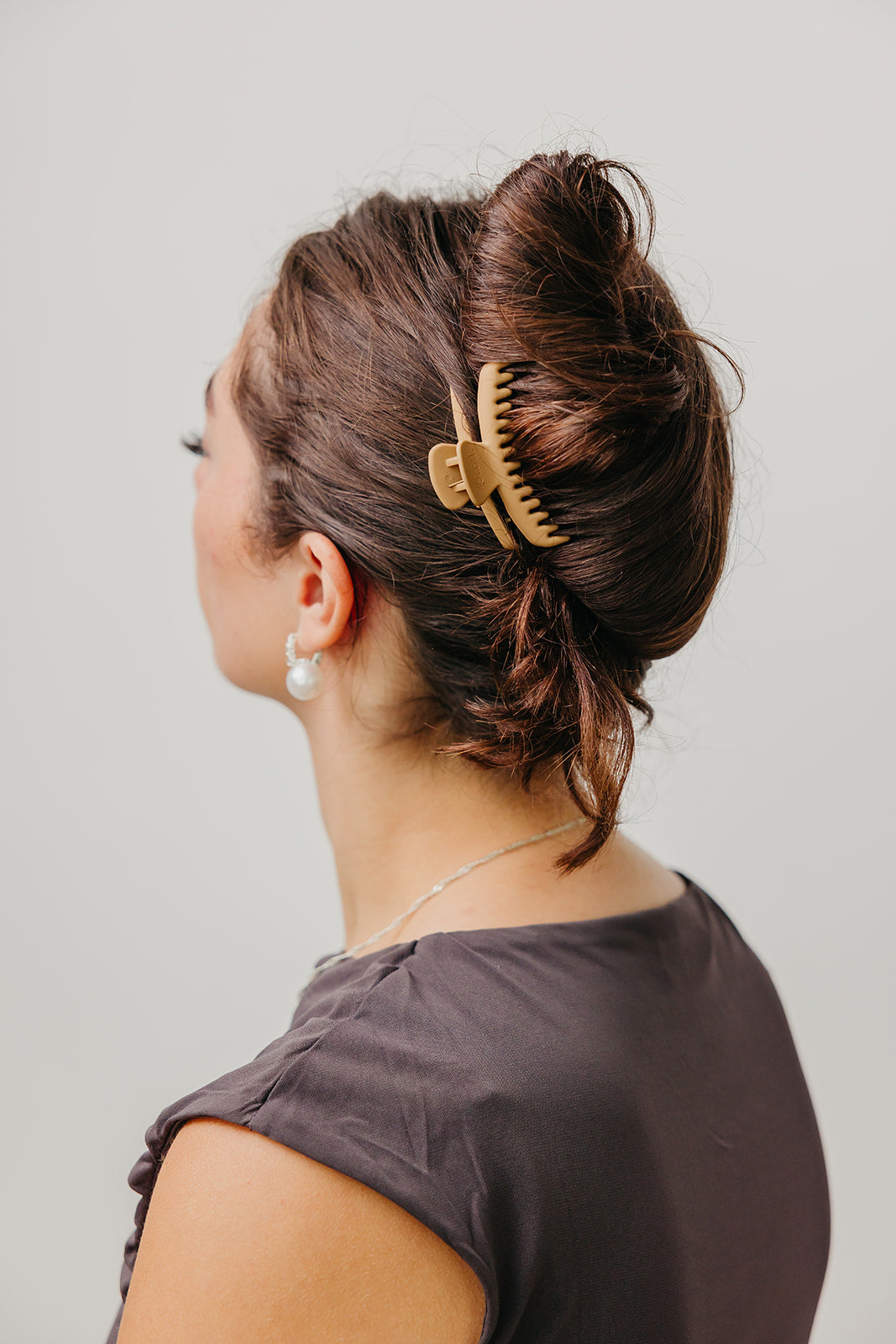 Beige matte claw hair clip securing dark hair in a high bun.