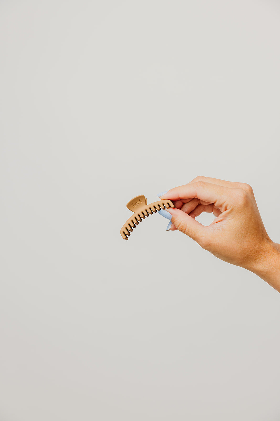 Mini matte hair claw clip in light brown, held in hand
