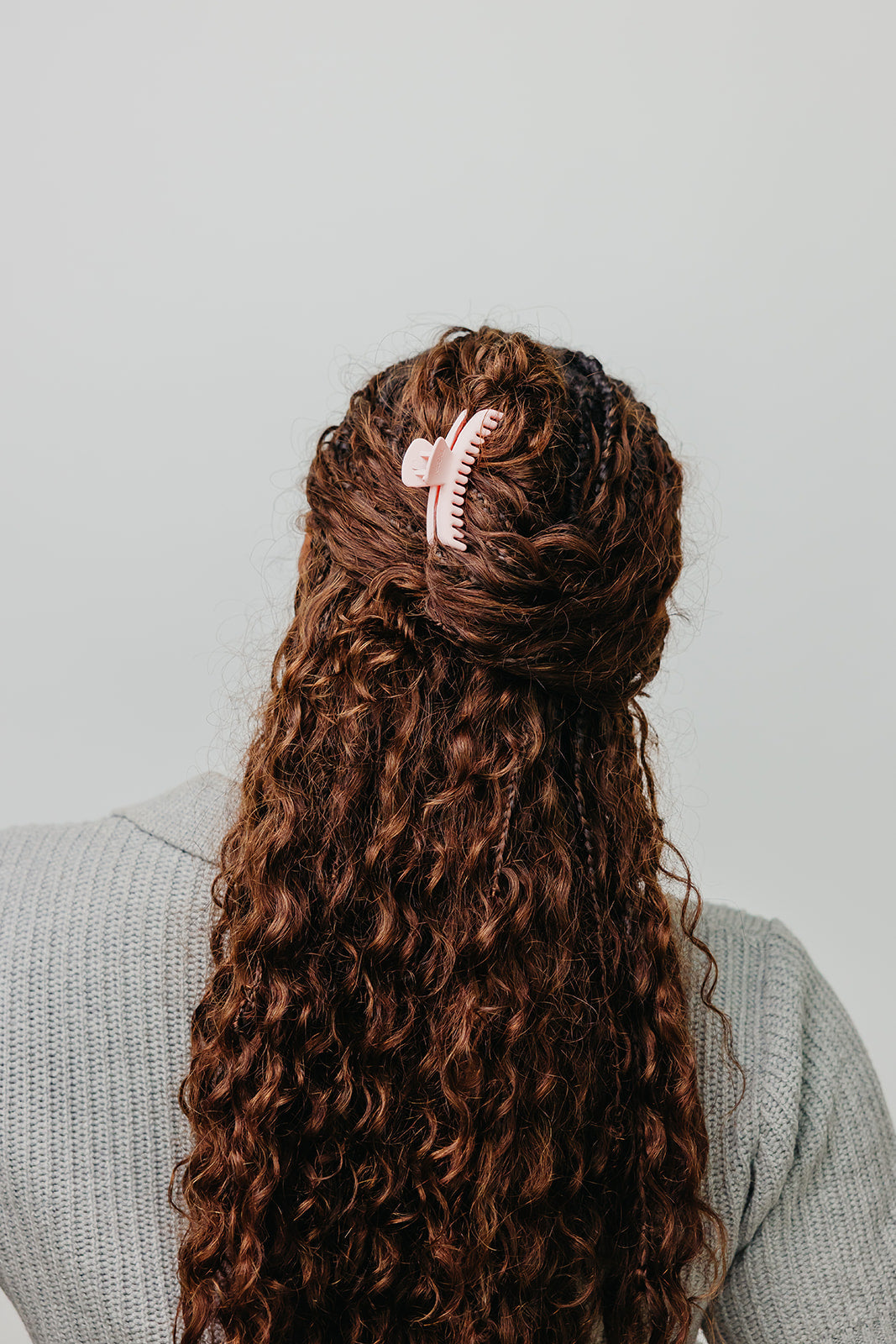 Pink matte mini claw hair clip securing dark curly hair back.