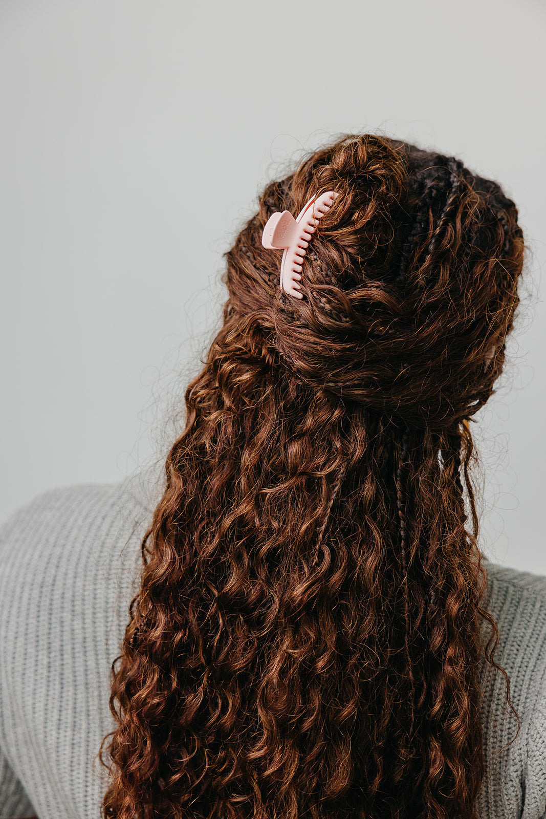 White matte mini claw hair clip holding dark curly hair back.