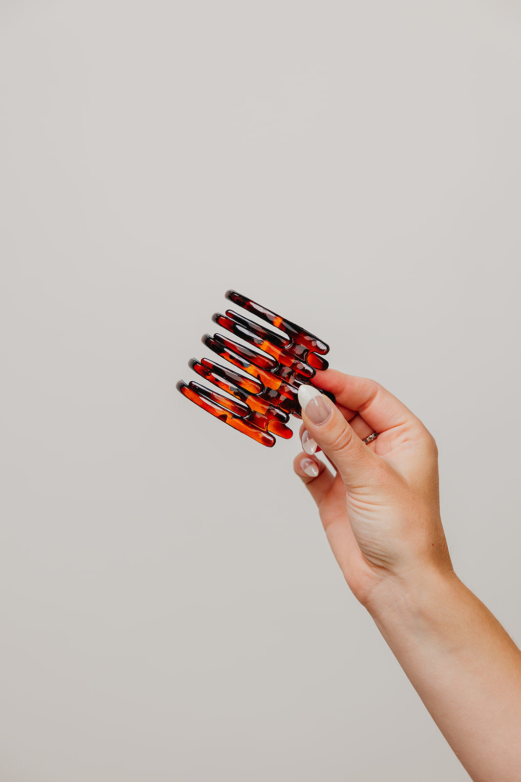 Wide hair claw clip in red-and-dark tortoise pattern, held in hand