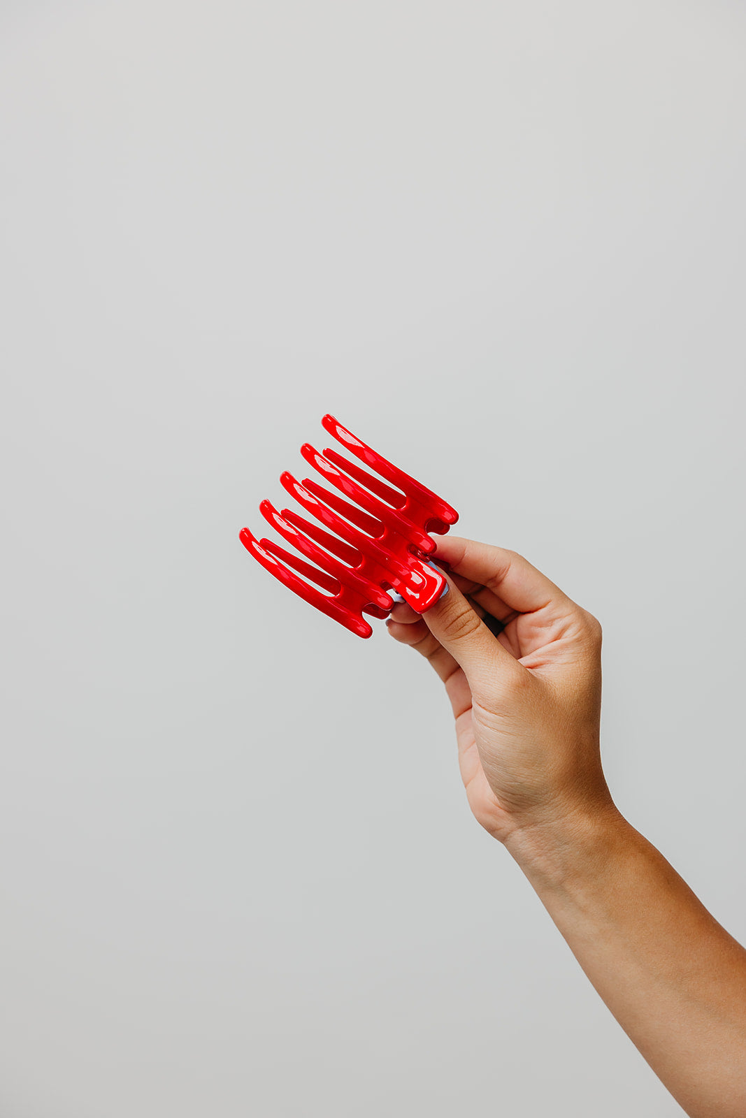 Hand holding a shiny red wide hair claw with five teeth