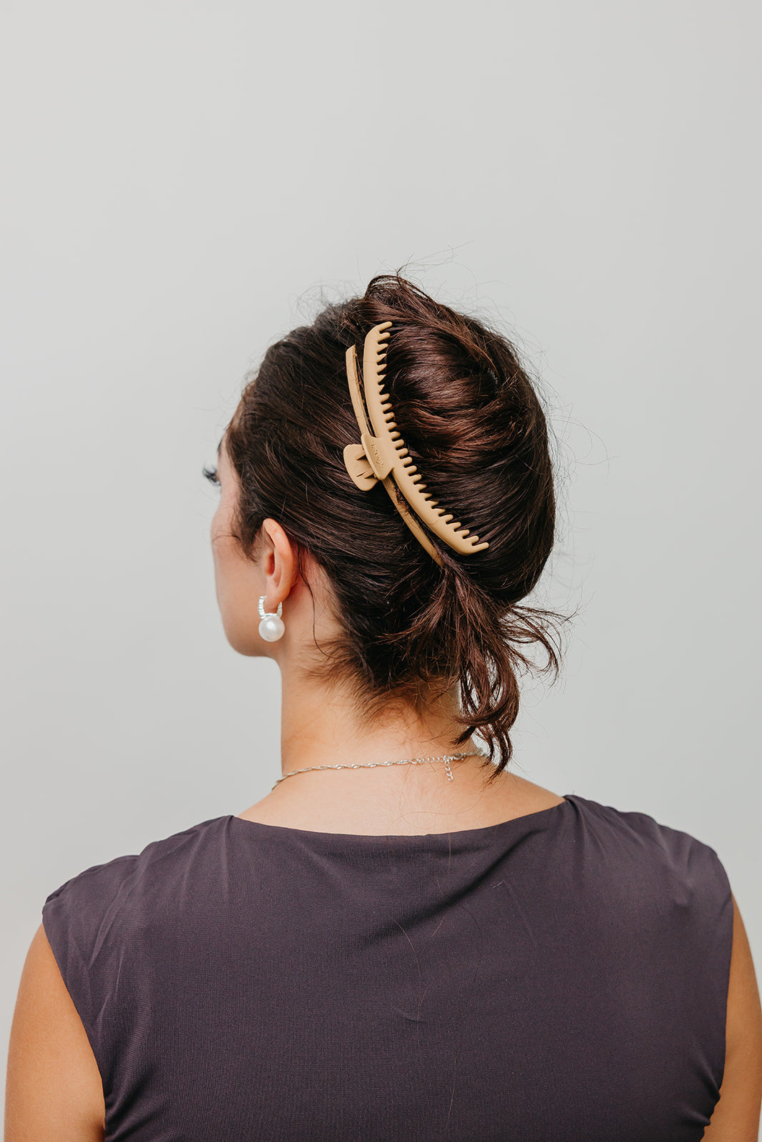 Beige matte claw hair clip in dark hair, back view with low bun