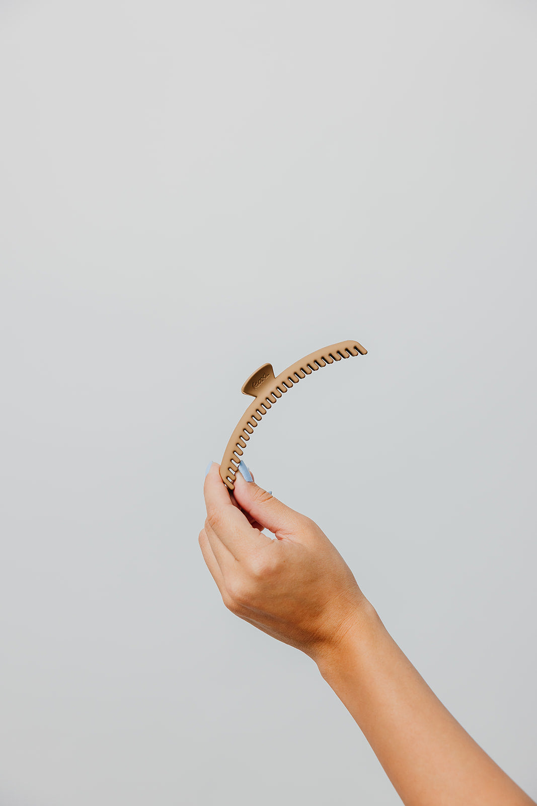 Matte hair claw clip with comb teeth, held in hand, tan/beige color.