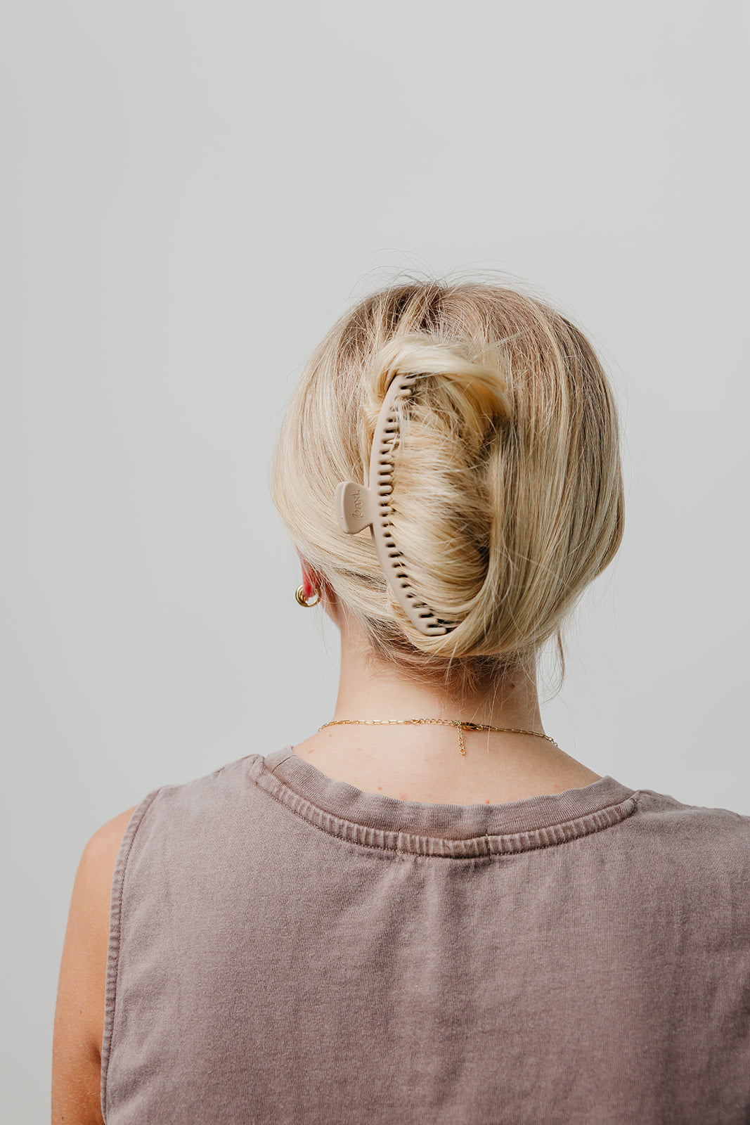 Matte hair claw clip in blonde hair, back view, holding hair up; mauve sleeveless top.