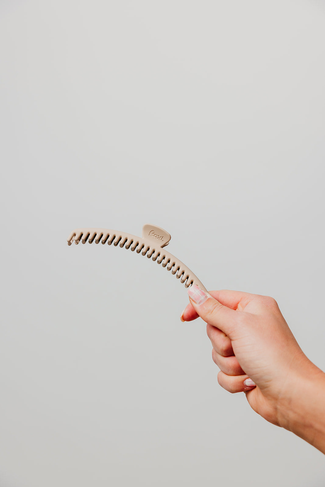 Matte hair claw clip with comb teeth, held in hand, tan/beige color.