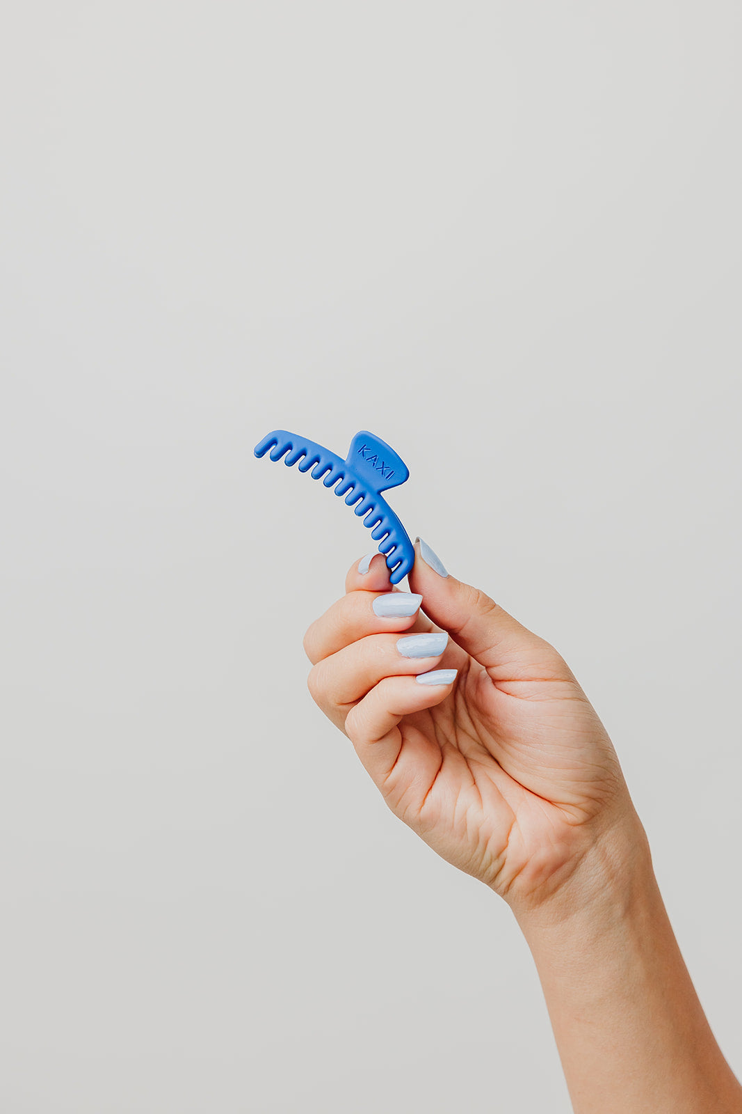 Blue matte mini claw hair clip with teeth, held in a hand.