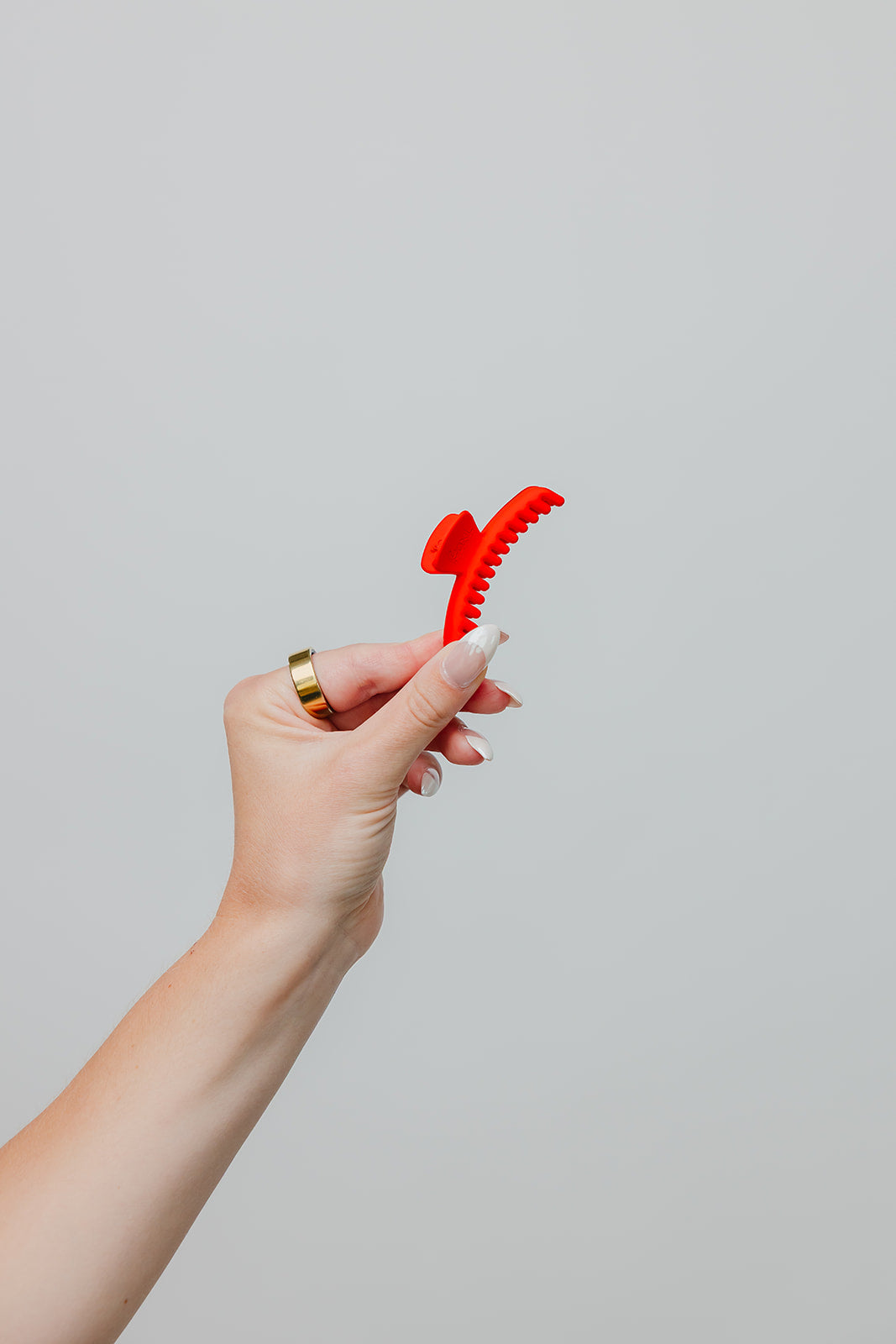 Orange-red matte mini claw hair clip held between fingers.