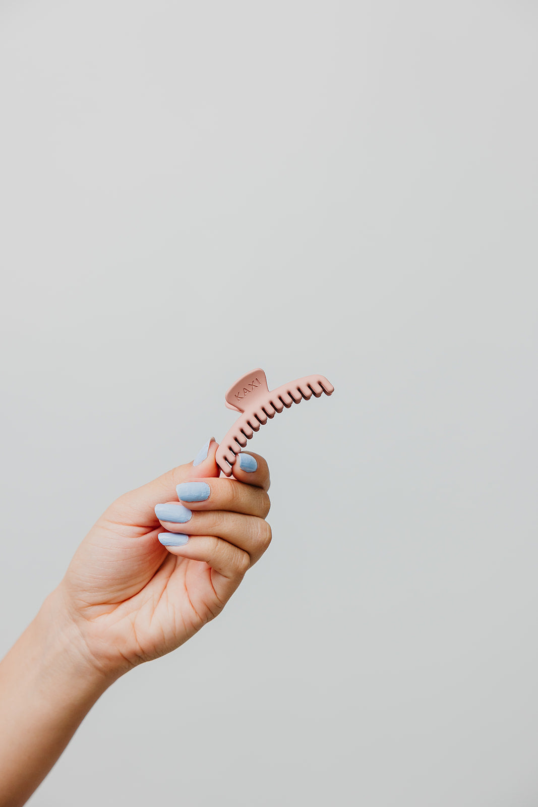 Mini matte hair claw clip in blush pink, held in hand