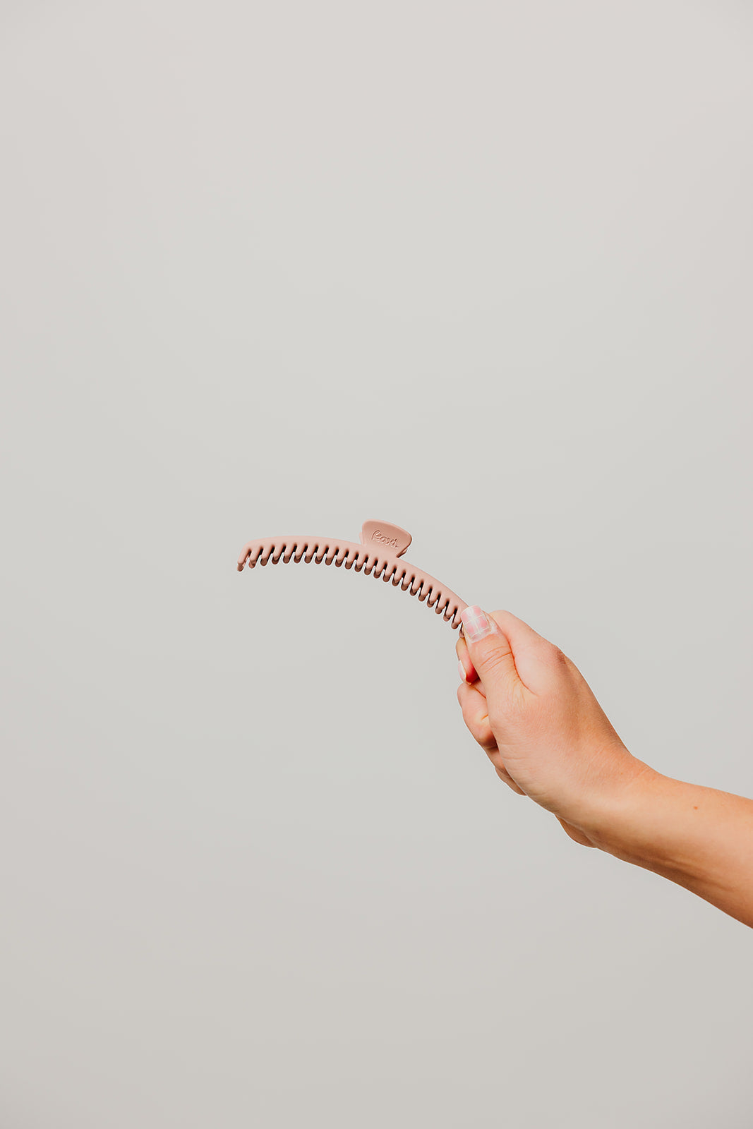 Matte hair claw clip with comb teeth, hand holding, tan/beige color.